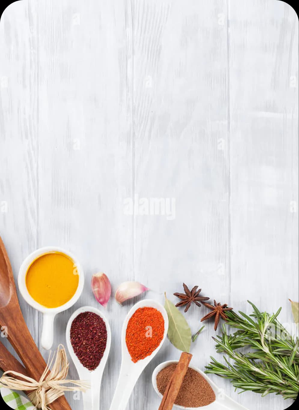 Spices, garlic, and herbs arranged on pale wood